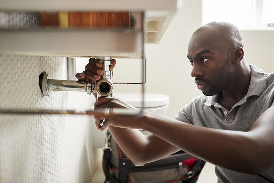 Plumbing Contractor Insurance - Closeup of a Male Plumber Sitting on the Floor and Fixing a Bathroom Sink